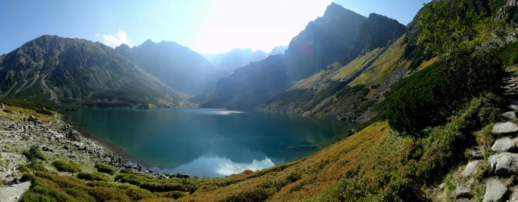 Panoramic view of a serene mountain lake surrounded by majestic peaks and sunlight.